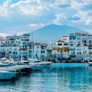 Yates de lujo en el puerto deportivo de Puerto Banús, con edificios blancos y montañas de fondo bajo un cielo azul, que ilustran el atractivo de la alta gama para la inversión inmobiliaria en España.