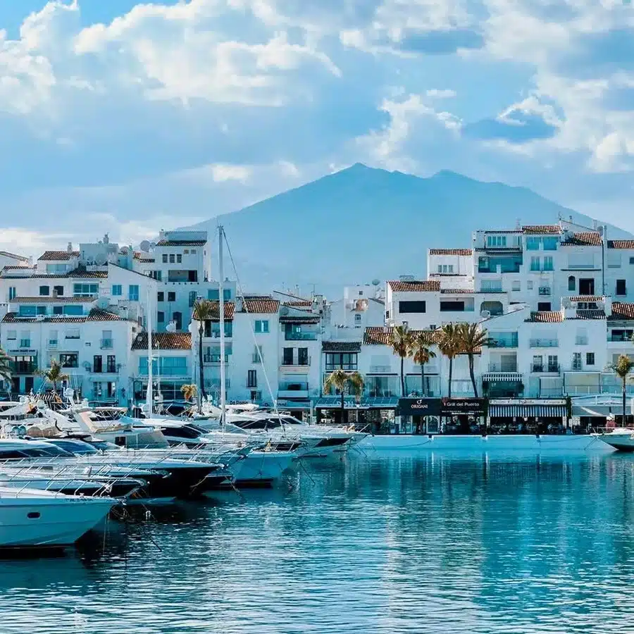 Yates de lujo en el puerto deportivo de Puerto Banús, con edificios blancos y montañas de fondo bajo un cielo azul, que ilustran el atractivo de la alta gama para la inversión inmobiliaria en España.
